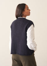 Woman wearing a dark navy blue sleeveless chunky knit waistcoat with green trousers and a white shirt