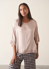 Woman wearing pearlescent light lilac satin top with navy check trousers and a dark plum chunky cardigan