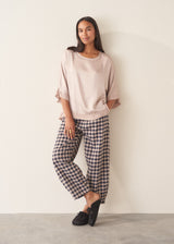 Woman wearing pearlescent light lilac satin top with navy check trousers and a dark plum chunky cardigan