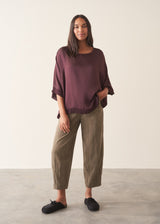 A woman wearing a plum satin top with khaki green trousers