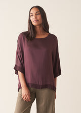 A woman wearing a plum satin top with khaki green trousers