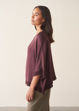 A woman wearing a plum satin top with khaki green trousers