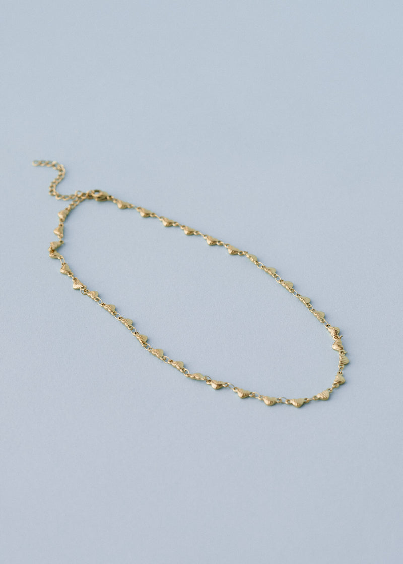 A gold chain link necklace with heart-shaped charms, on a blue background