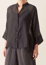 Woman wearing semi-sheer button up black shirt with dark grey wide leg trousers. 