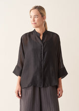 Woman wearing semi-sheer button up black shirt with dark grey wide leg trousers. 