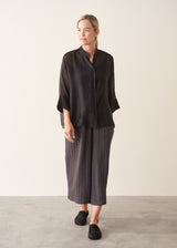 Woman wearing semi-sheer button up black shirt with dark grey wide leg trousers. 
