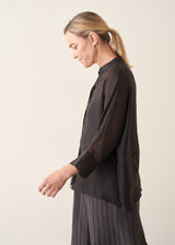 Woman wearing semi-sheer button up black shirt with dark grey wide leg trousers. 