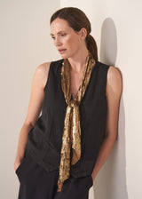 Woman wearing black waistcoat and gold sequin scarf against a plain background.