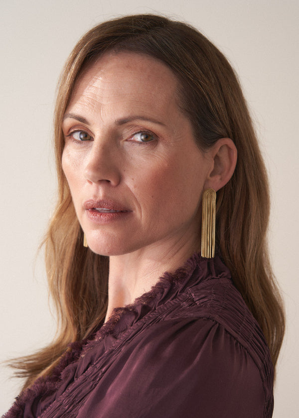 Woman wearing gold chain tassel earrings and beige background