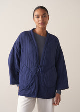 Person wearing a navy blue jacket and white barrel leg trousers against a plain background