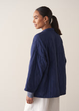 Person wearing a navy blue jacket and white barrel leg trousers against a plain background