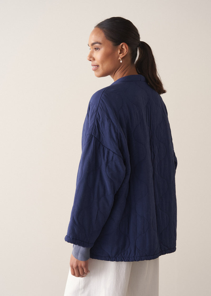 Person wearing a navy blue jacket and white barrel leg trousers against a plain background