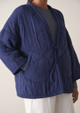 Person wearing a navy blue jacket and white barrel leg trousers against a plain background