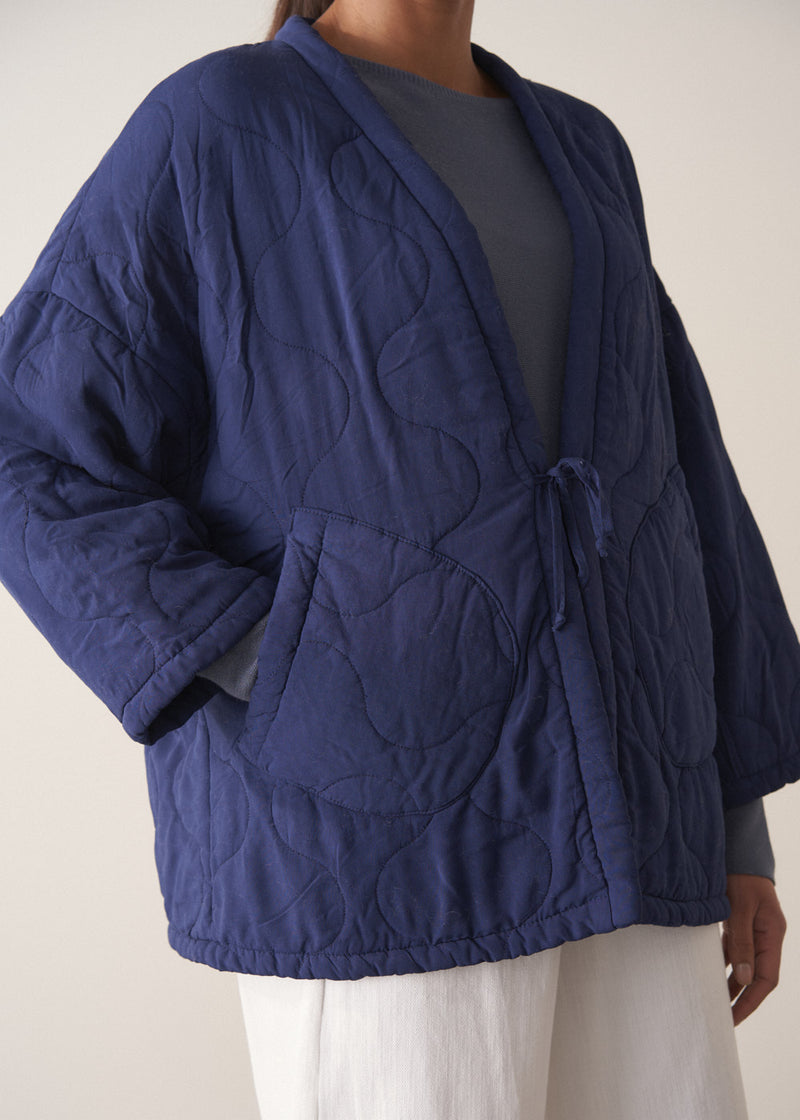 Person wearing a navy blue jacket and white barrel leg trousers against a plain background