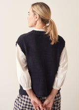 Woman wearing dark blue chunk knit waistcoat with white shirt and blue checked trousers