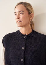 Woman wearing dark blue chunk knit waistcoat with white shirt and blue checked trousers