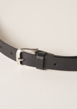 Close up of a black real leather belt with a brushed silver buckle, on a beige background