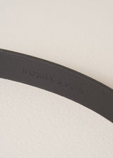 Close up of a black real leather belt with "Busby & Fox" branding debossed into the leather, on a beige background