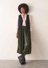 Woman wearing green velvet cropped wide-leg trousers and a pink shirt against a plain background