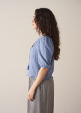 Woman wearing blue textured blouse with tassels and grey stripe trousers