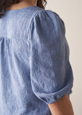 Woman wearing blue textured blouse with tassels and grey stripe trousers