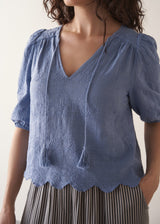Woman wearing blue textured blouse with tassels and grey stripe trousers