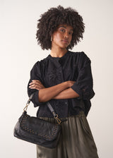 Woman holding a black handbag against a plain background