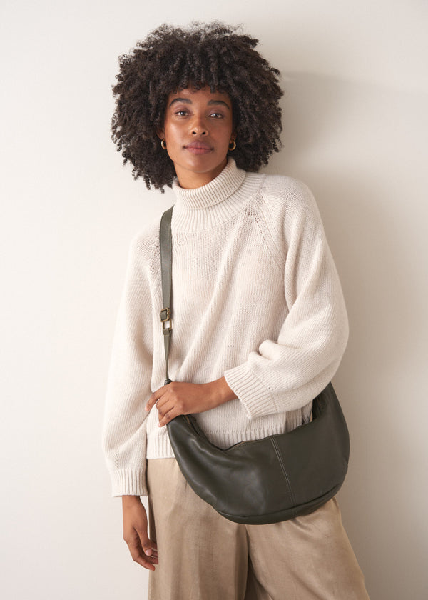 Woman holding a khaki leather bag against a plain background