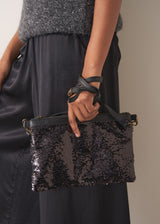 Person holding a black sequined handbag against a neutral background