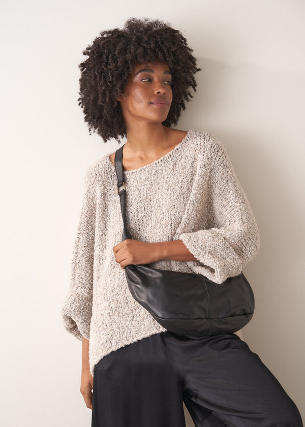Woman wearing a textured sweater and carrying a black leather bag against a plain background
