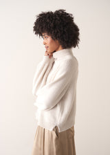 Woman wearing a white rollneck sweater and beige wide leg trousers against a white background
