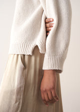 Woman wearing a white rollneck sweater and beige wide leg trousers against a white background