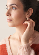 Woman wearing gold plated, beaded drop stud earrings with striped red and pink cardigan, against a beige background