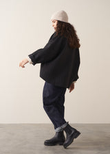 Woman wearing a black quilted kimono jacket over a beige sweater and dark jeans against a plain background