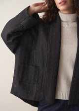 Woman wearing a black quilted kimono jacket over a beige sweater and dark jeans against a plain background