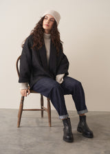 Woman wearing a black quilted kimono jacket over a beige sweater and dark jeans against a plain background