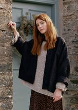 Woman leant against a stone wall, wearing a oversized quilted jacket over a beige jumper and leopard print skirt