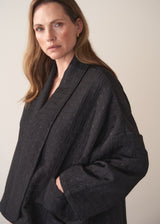 Woman wearing a oversized quilted jacket over a white top and gold trousers against a light background