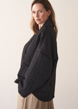 Woman wearing a oversized quilted jacket over a white top and gold trousers against a light background