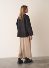 Woman wearing a oversized quilted jacket over a white top and gold trousers against a light background