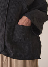 Woman wearing a oversized quilted jacket over a white top and gold trousers against a light background