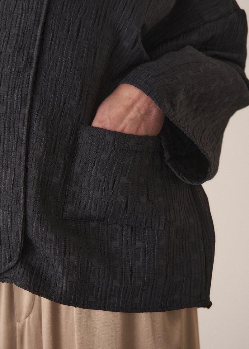 Woman wearing a oversized quilted jacket over a white top and gold trousers against a light background