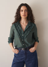 Woman wearing dark green ruffle front shirt with blue jeans