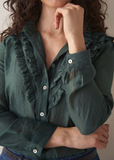 Woman wearing dark green ruffle front shirt with blue jeans