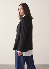Woman wearing black oversized floppy jacket with a white shirt and blue jeans.
