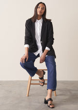 Woman wearing black oversized floppy jacket with a white shirt and blue jeans.