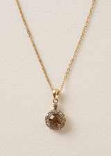 A close up of a delicate gold chain necklace which features a pendant adorned with sparkling silver diamantes and a rich, amber-coloured crystal.