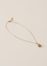 A delicate gold chain necklace which features a pendant adorned with sparkling silver diamantes and a rich, amber-coloured crystal, on a beige background