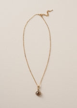 A delicate gold chain necklace which with pendant adorned with sparkling silver diamantes and a rich, amber-coloured crystal, on a beige background
