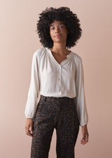 Woman wears a long sleeve blouse in oatmeal tucked into leopard print trousers